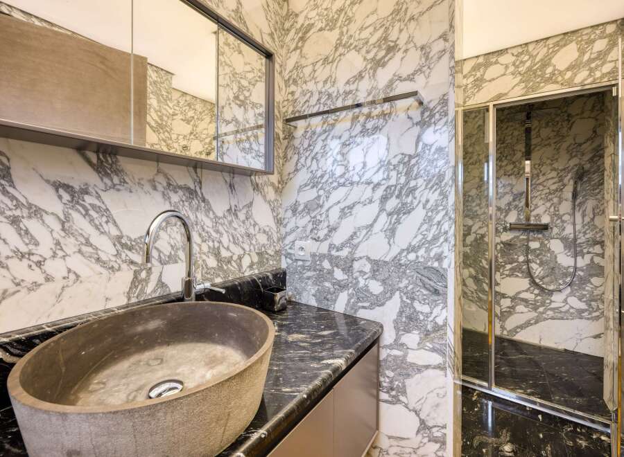 This luxurious bathroom boasts a stunning marble design, featuring a spacious walk-in shower with glass enclosure and a sleek, modern sink.