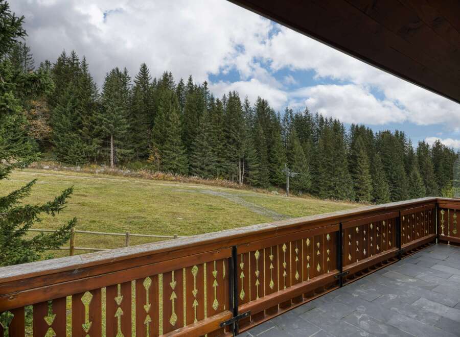 This stunning property boasts a spacious balcony with a wooden railing, offering breathtaking views of a lush green landscape and a dense forest.