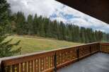 This stunning property boasts a spacious balcony with a wooden railing, offering breathtaking views of a lush green landscape and a dense forest.