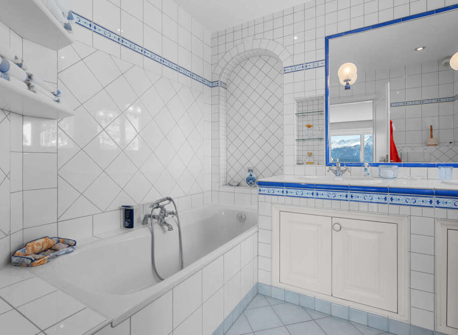 This luxurious bathroom boasts a classic white and blue tile design, complete with a built-in bathtub and spacious vanity.