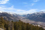 Breathtaking panoramic view of a snow-capped mountain range and valley, showcasing a picturesque landscape with a dense forest in the foreground.