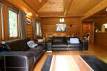 Cozy log cabin living room with leather sofas, a wood dining table, and large windows offering scenic views.