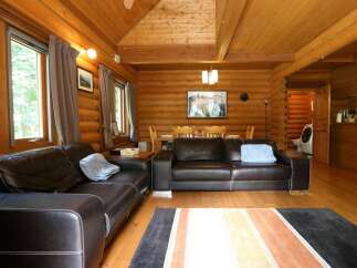 Cozy log cabin living room with leather sofas, a wood dining table, and large windows offering scenic views.