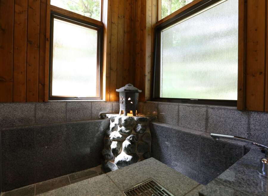 Relax and rejuvenate in this luxurious bathroom, featuring a serene stone bath and stunning natural light from large windows.