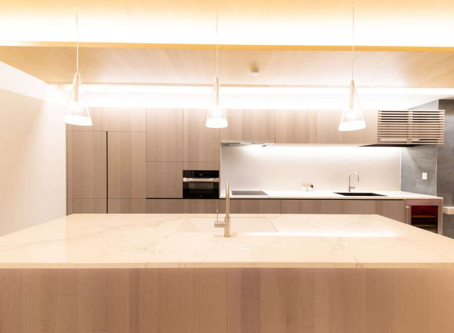 Modern kitchen with sleek light wood cabinetry, marble countertops, and integrated appliances.