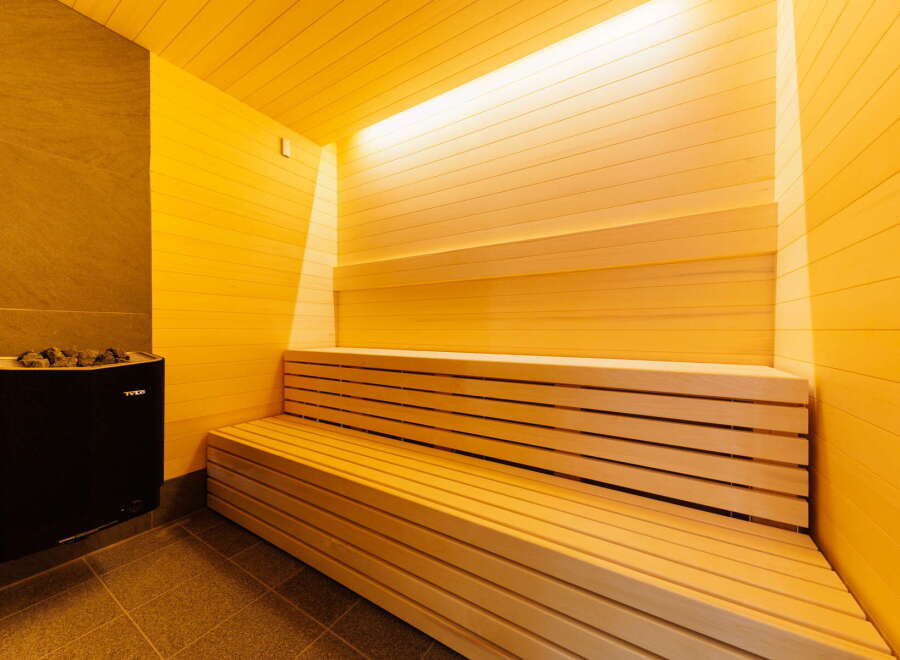 Indulge in ultimate relaxation in this exquisite sauna, featuring a spacious wooden bench and a sleek, modern heater.