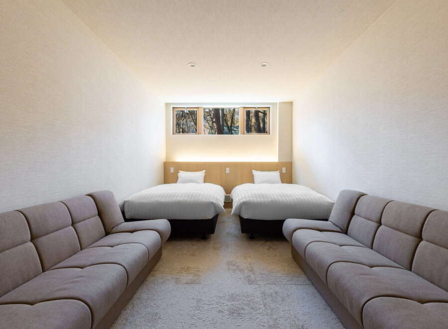 Relax in this serene hotel room featuring two comfy twin beds and two plush sofas, perfect for a family getaway.