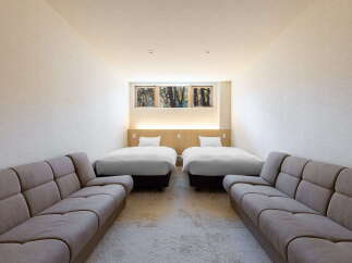 Relax in this serene hotel room featuring two comfy twin beds and two plush sofas, perfect for a family getaway.