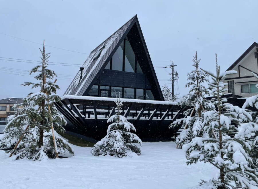 A frame A-frame house nestled in a snowy landscape.
