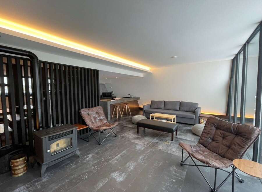 Modern living space with a wood-burning stove, comfortable leather armchairs, and a sleek sofa.