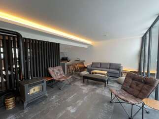 Modern living space with a wood-burning stove, comfortable leather armchairs, and a sleek sofa.