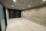 Modern minimalist garage with sleek black roll-up door and polished concrete floor.
