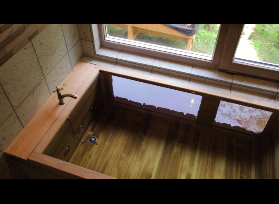Indulge in tranquility with this exquisite wooden bathtub, perfectly nestled near a window offering serene garden views.