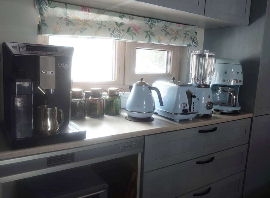 This stunning kitchen boasts a full suite of high-end appliances, including a DeLonghi espresso machine, Smeg coffee maker, and stylish pastel-colored kettle and toaster.