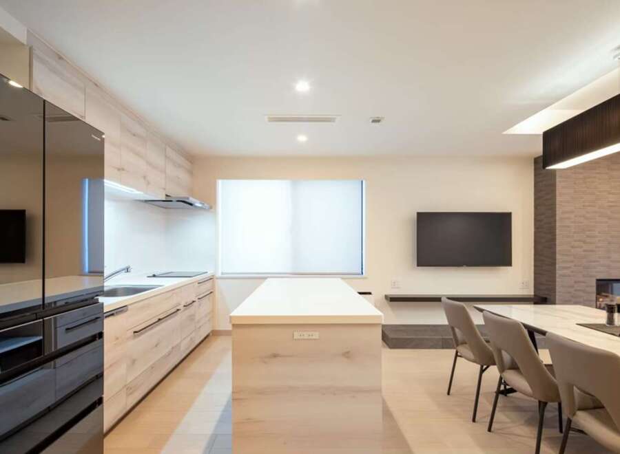 Modern kitchen with sleek black appliances and light wood cabinetry opens to a dining area with a marble table and comfortable seating.