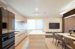 Modern kitchen with sleek black appliances and light wood cabinetry opens to a dining area with a marble table and comfortable seating.