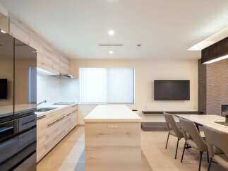 Modern kitchen with sleek black appliances and light wood cabinetry opens to a dining area with a marble table and comfortable seating.