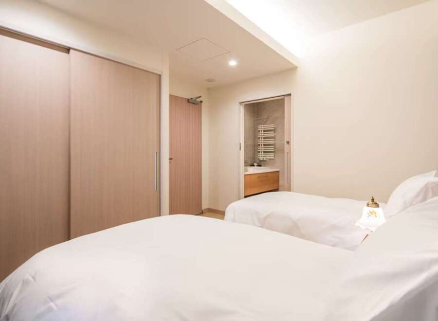 This luxurious bedroom features twin beds with crisp white linens, a built-in closet with sliding doors, and an ensuite bathroom with modern fixtures.