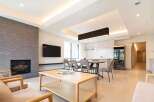 Modern living space with open-plan kitchen and dining area, featuring a sleek fireplace and large windows.