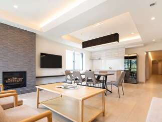 Modern living space with open-plan kitchen and dining area, featuring a sleek fireplace and large windows.
