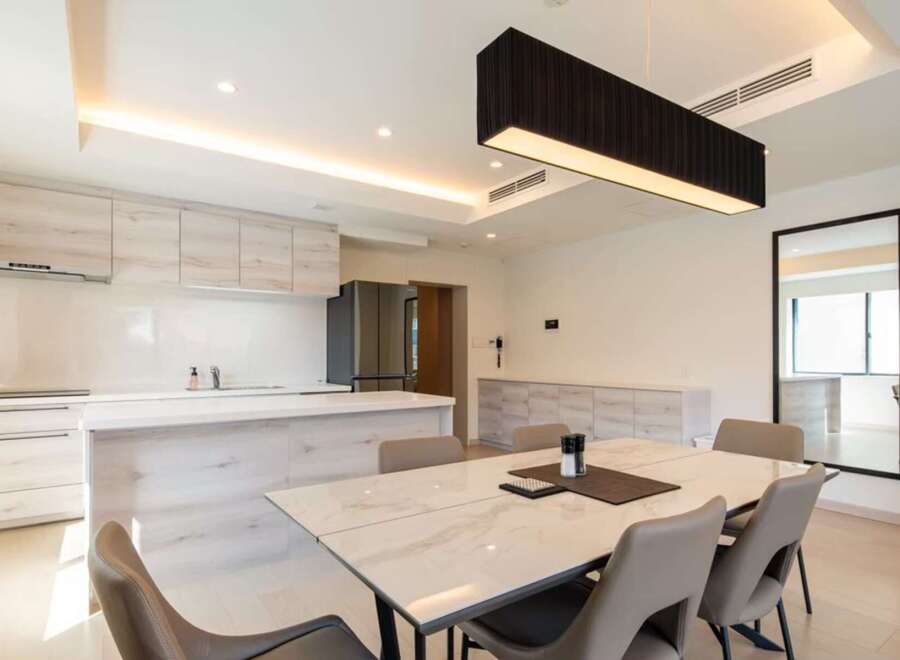 Modern kitchen with sleek cabinetry and island, open to a dining area with marble table and six chairs.