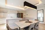 Modern kitchen with sleek cabinetry and island, open to a dining area with marble table and six chairs.