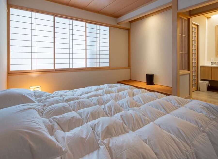 Experience serene living in this exquisitely designed bedroom, featuring a plush, white comforter and traditional Japanese shoji screens that filter soft, natural light.