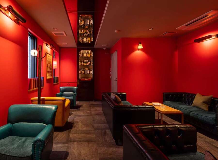 Luxurious red-walled lounge with plush leather seating and a built-in bar showcasing an impressive liquor collection.