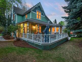 This charming green house boasts a spacious wrap-around porch, perfect for enjoying evenings outdoors.