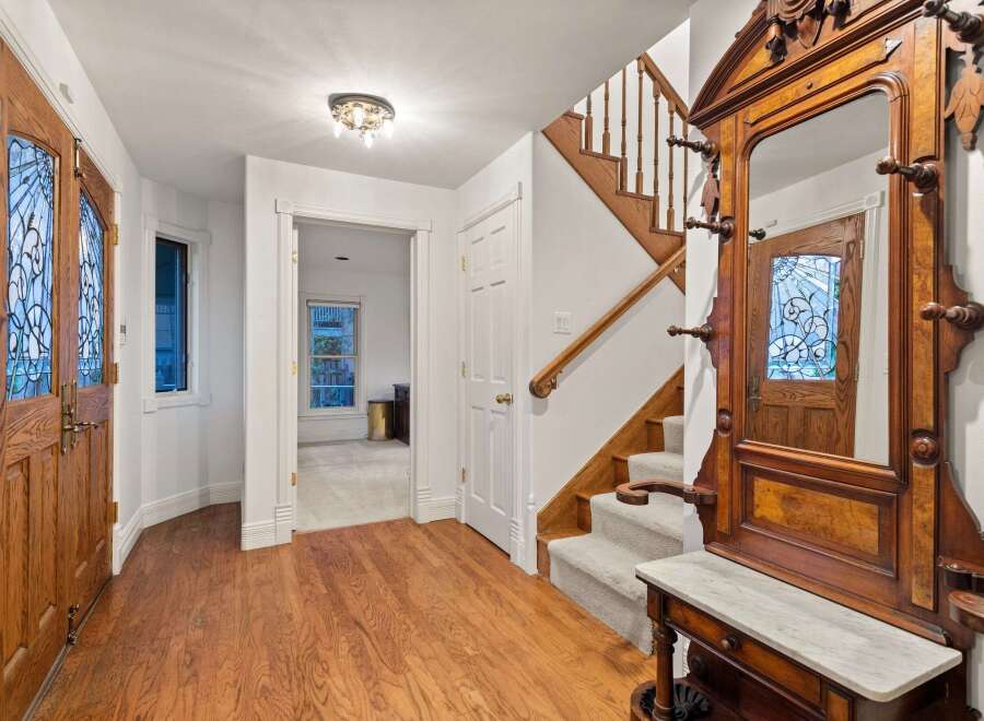 This stunning entryway boasts gleaming hardwood floors, an antique hall tree, and elegant stained-glass doors.