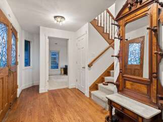 This stunning entryway boasts gleaming hardwood floors, an antique hall tree, and elegant stained-glass doors.