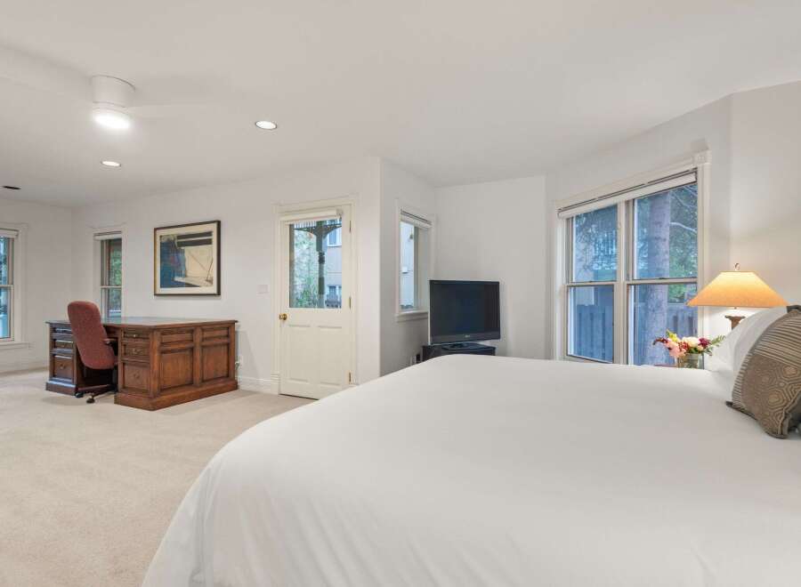 Bright and spacious bedroom with a comfortable king-size bed, large windows offering natural light, and a convenient workspace with a wooden desk and chair.
