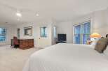 Bright and spacious bedroom with a comfortable king-size bed, large windows offering natural light, and a convenient workspace with a wooden desk and chair.