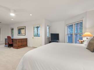 Bright and spacious bedroom with a comfortable king-size bed, large windows offering natural light, and a convenient workspace with a wooden desk and chair.