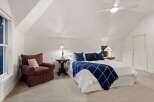 Relax in this serene bedroom, featuring a cozy armchair and a plush bed with a navy blue throw.