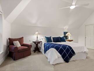 Relax in this serene bedroom, featuring a cozy armchair and a plush bed with a navy blue throw.