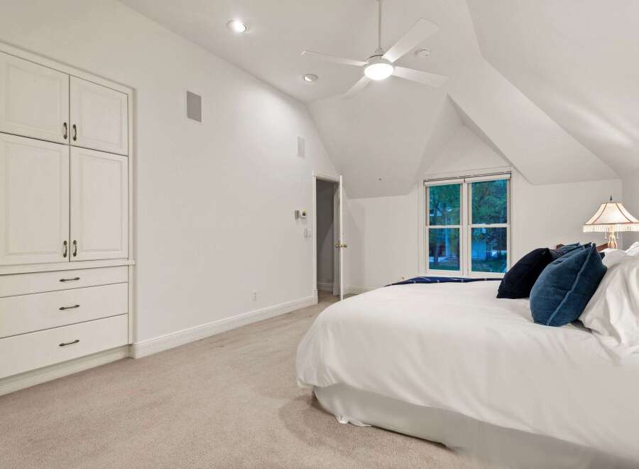 This bright and airy bedroom boasts a vaulted ceiling, complemented by a ceiling fan for optimal comfort.