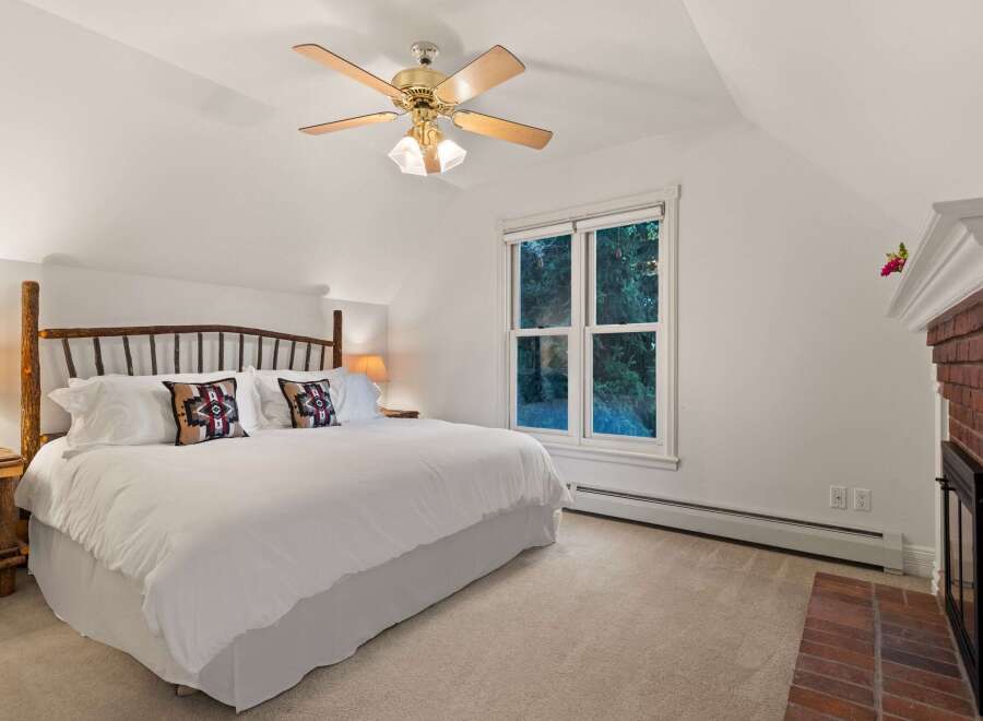 Relax in this cozy bedroom featuring a king-size bed, a ceiling fan, and a fireplace.