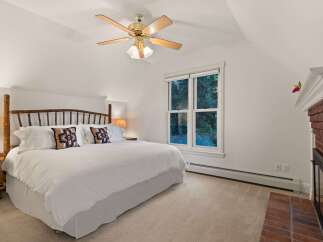 Relax in this cozy bedroom featuring a king-size bed, a ceiling fan, and a fireplace.