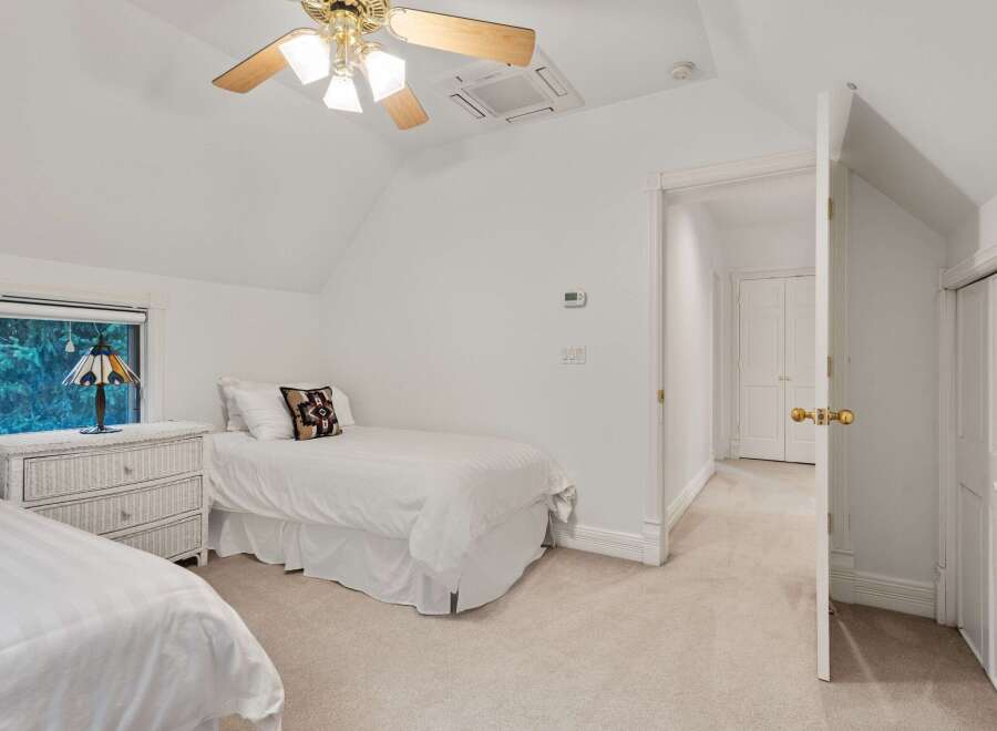 Charming bedroom with twin beds, white wicker dresser, and a ceiling fan.