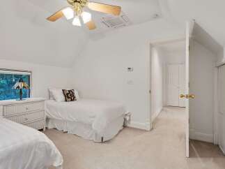Charming bedroom with twin beds, white wicker dresser, and a ceiling fan.