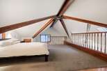 Cozy attic bedroom with exposed wooden beams and a loft area.