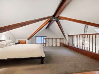 Cozy attic bedroom with exposed wooden beams and a loft area.