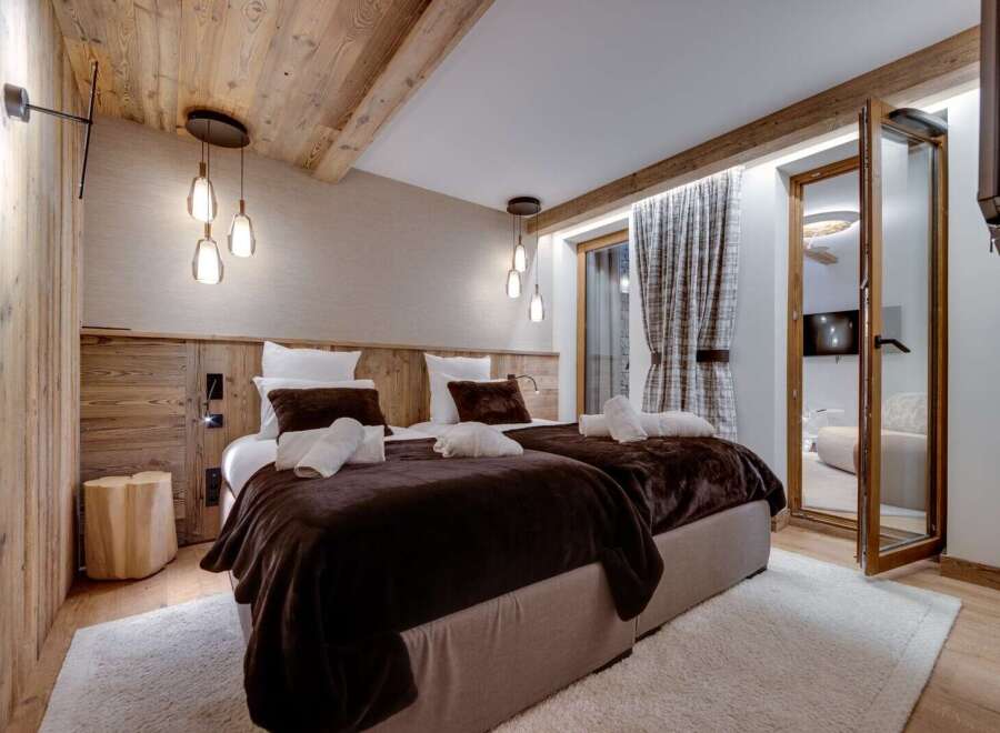 Cozy chalet bedroom with twin beds, wooden walls, and a plush brown throw.