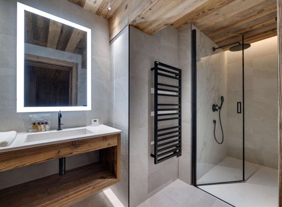 This stunning bathroom boasts a spacious shower with modern fixtures, a sleek floating vanity with wooden accents, and a large illuminated mirror.
