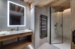 This stunning bathroom boasts a spacious shower with modern fixtures, a sleek floating vanity with wooden accents, and a large illuminated mirror.