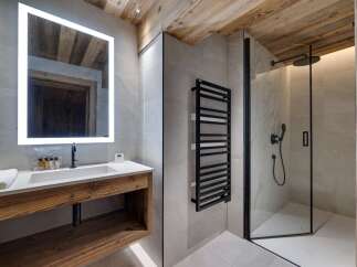 This stunning bathroom boasts a spacious shower with modern fixtures, a sleek floating vanity with wooden accents, and a large illuminated mirror.