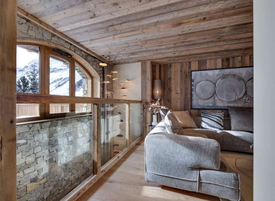 This stunning chalet boasts a breathtaking mountain view from its arched window, complemented by a rustic wooden ceiling and stone wall.