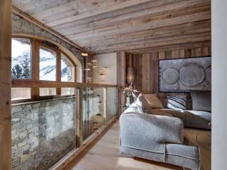 This stunning chalet boasts a breathtaking mountain view from its arched window, complemented by a rustic wooden ceiling and stone wall.