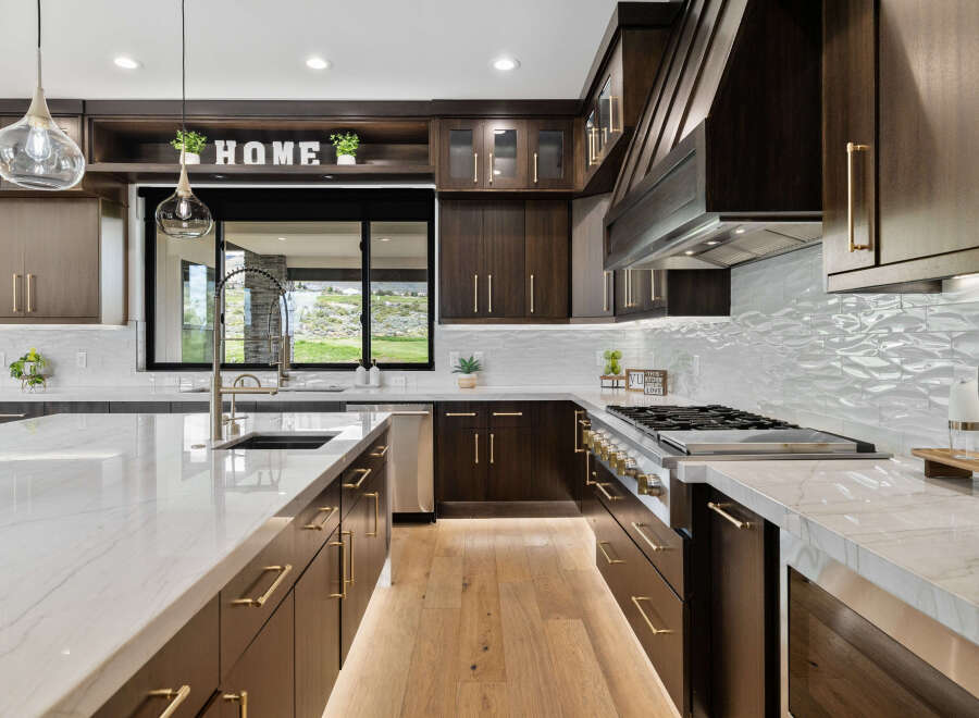 This stunning kitchen boasts a modern design with dark wood cabinetry, sleek gold hardware, and a large island with a marble countertop.